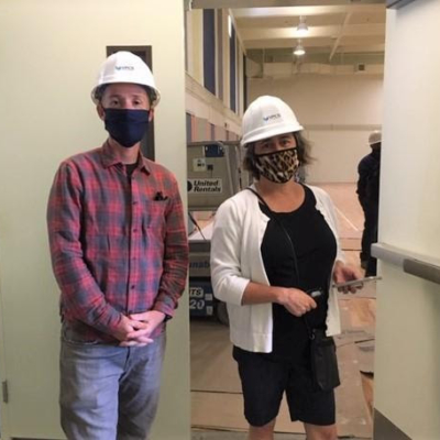 Two people standing side-by-side wearing masks and hardhats