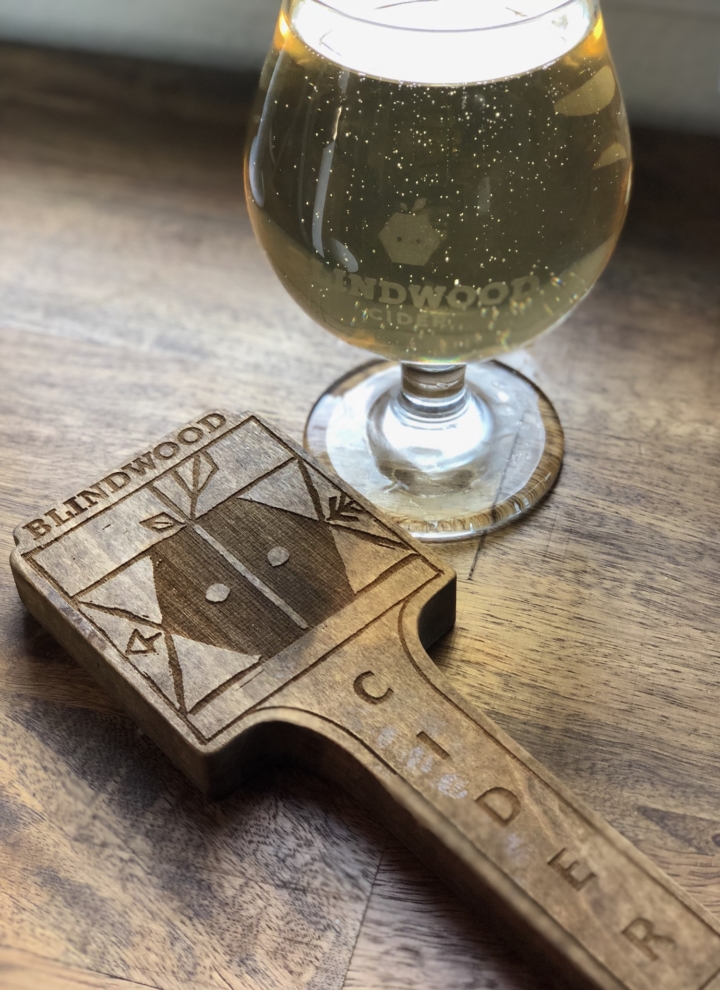 A glass of Blindwood cider and a Blindwood tap handle sit on a table.